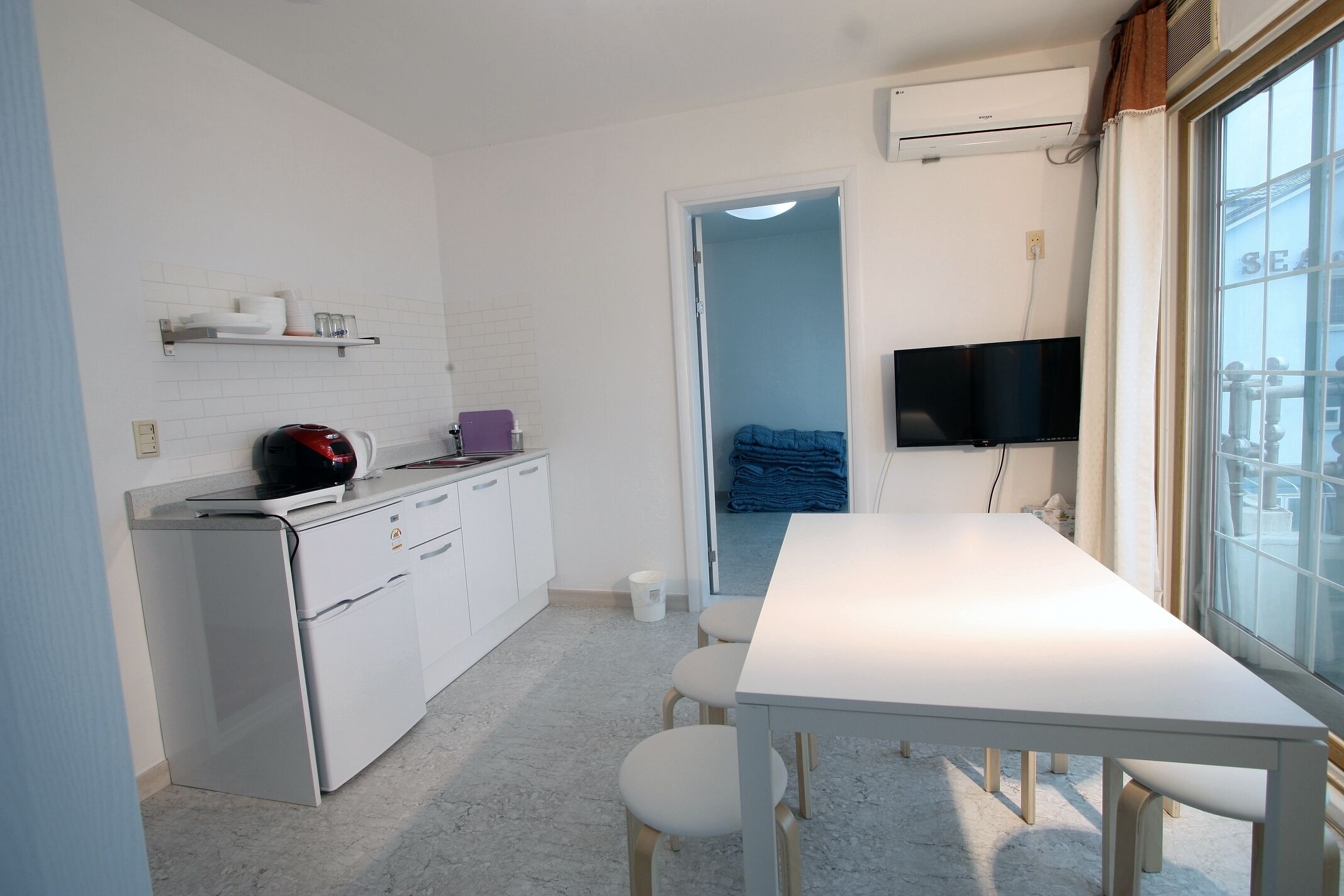 A compact kitchen with white cabinets, a small refrigerator, a coffee maker, and a TV mounted on the wall.