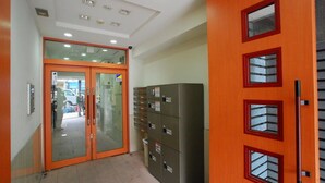 Un pasillo con puerta de vidrio, archivadores metálicos y ventana con marco rojo.