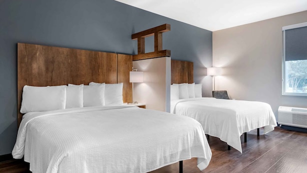 A hotel room with two beds, wooden headboards, a large window, and a wall-mounted air conditioning unit.
