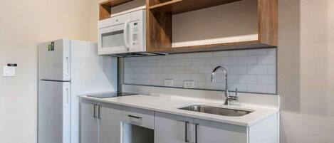 A compact kitchen with white cabinetry, a built-in microwave, and a stainless steel sink.