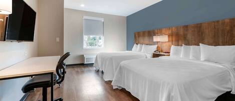 A hotel room with two beds, a desk, a chair, a TV, and a window.