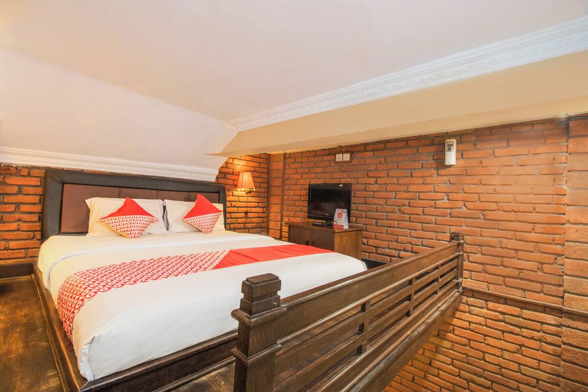 A hotel room with a brick wall, a wooden bed frame, and a television on a wooden stand.