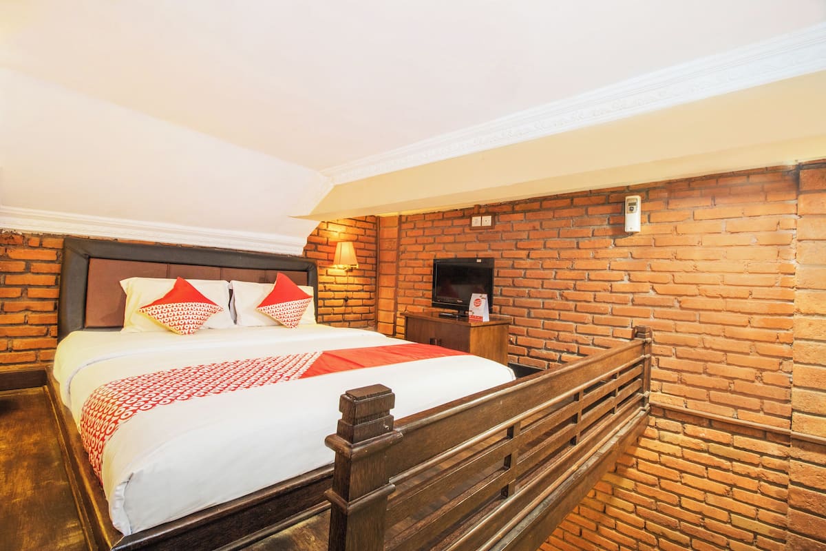 A hotel room with a brick wall, a wooden bed frame, a television, and a nightstand.