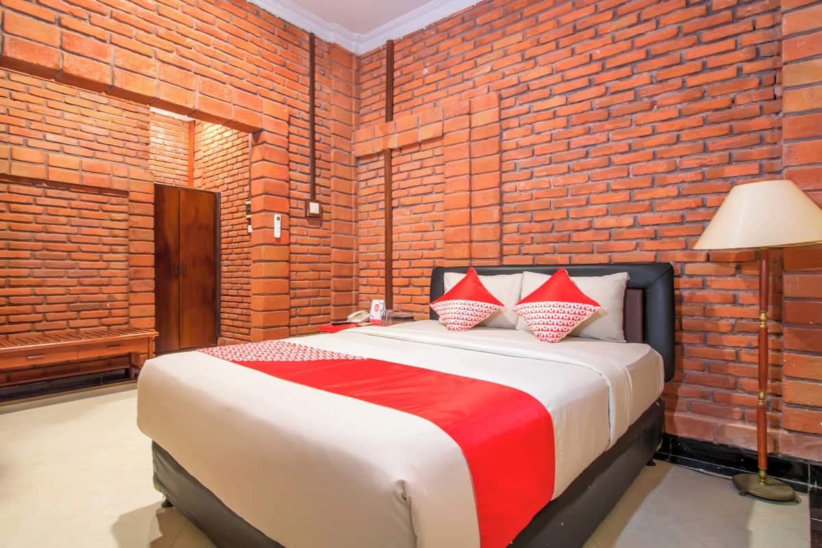 A hotel room with a brick wall, a bed with a red and white bedspread, and a lamp.