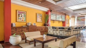 A hotel lobby with a wooden ceiling, yellow walls, a reception desk, a sofa, a coffee table, and a bar area with stools. - Hotel O Maxi Budget (Kuta)