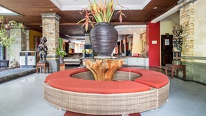 A lobby with a circular wicker sofa, a large planter, and a stone pillar. - Hotel O Maxi Budget (Kuta)