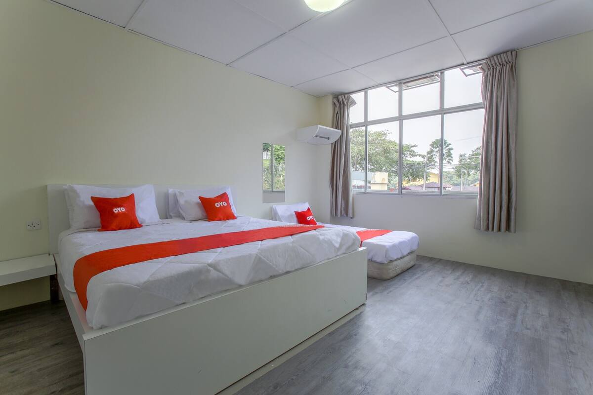 Ein Hotelzimmer mit einem großen Bett, einem kleineren Bett und einem Fenster mit Vorhängen.