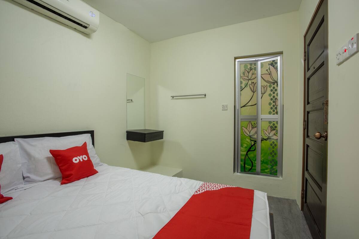 Ein Hotelzimmer mit Bett, Nachttisch, Spiegel, Fenster mit floralem Dekor und Klimaanlage.