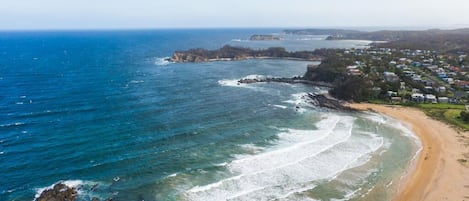 Eine Küstenlandschaft mit Sandstrand, felsiger Uferlinie und einer Wohngegend mit Häusern.