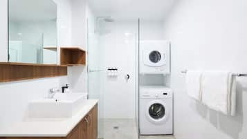 Un baño moderno con lavamanos, espejo, armarios de madera, cabina de ducha de vidrio y lavadora y secadora apiladas.