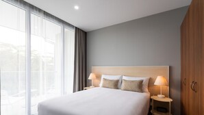 A hotel room with a large bed, two bedside tables with lamps, a wardrobe, and a large window with curtains. - Abode Hotel Malua Bay (Malua Bay)