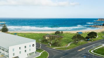 A coastal road with a beach in the background, a modern building with a flat roof, and a clear sky.