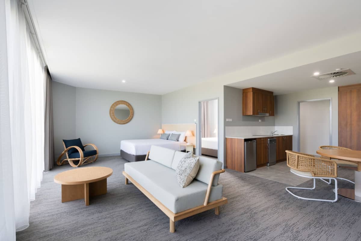Une chambre d’hôtel moderne comprenant un canapé, deux lits simples, une table à manger, un coin cuisine et une salle de bain.