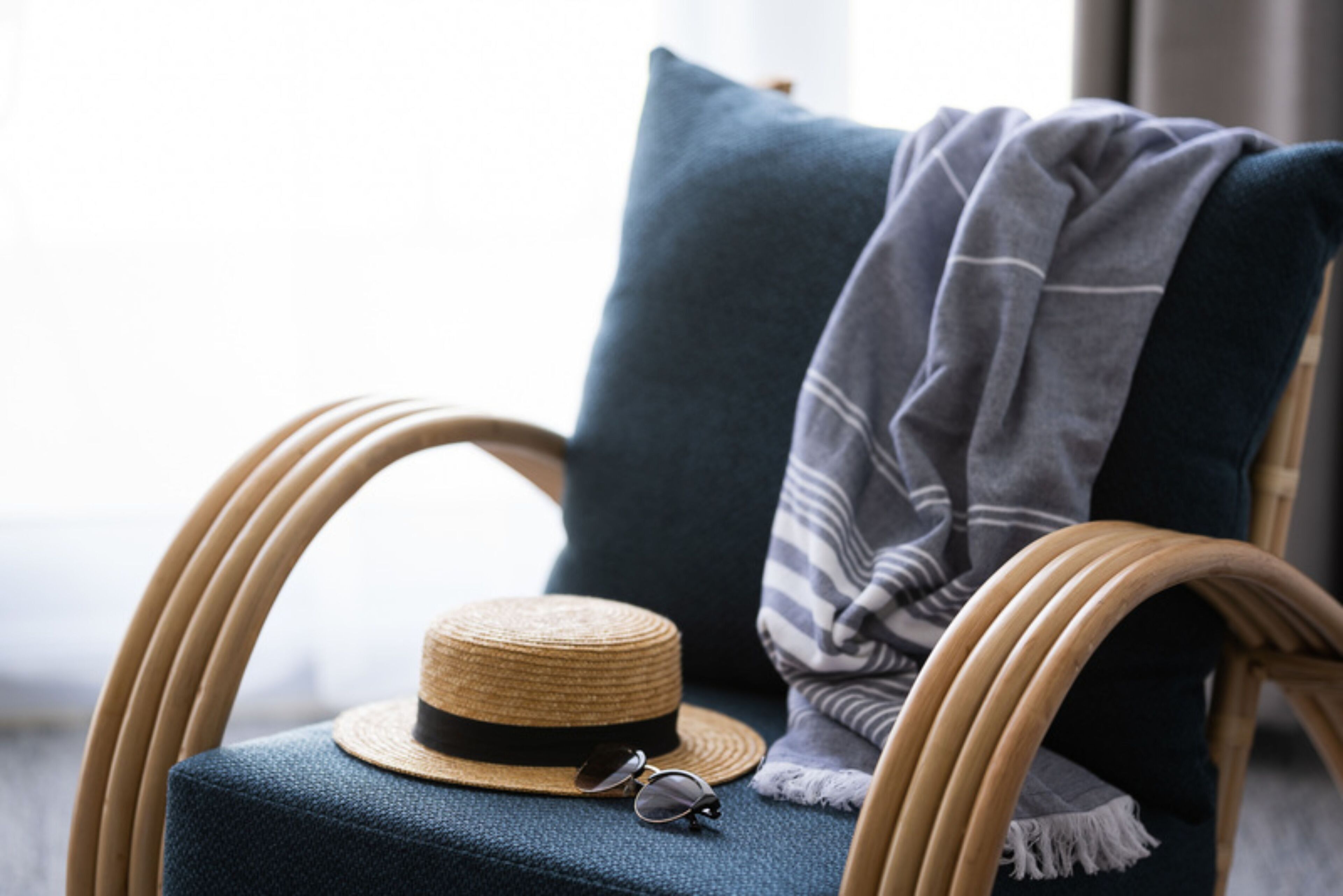 A wicker chair with a dark blue cushion, a straw hat, and a pair of sunglasses on it.