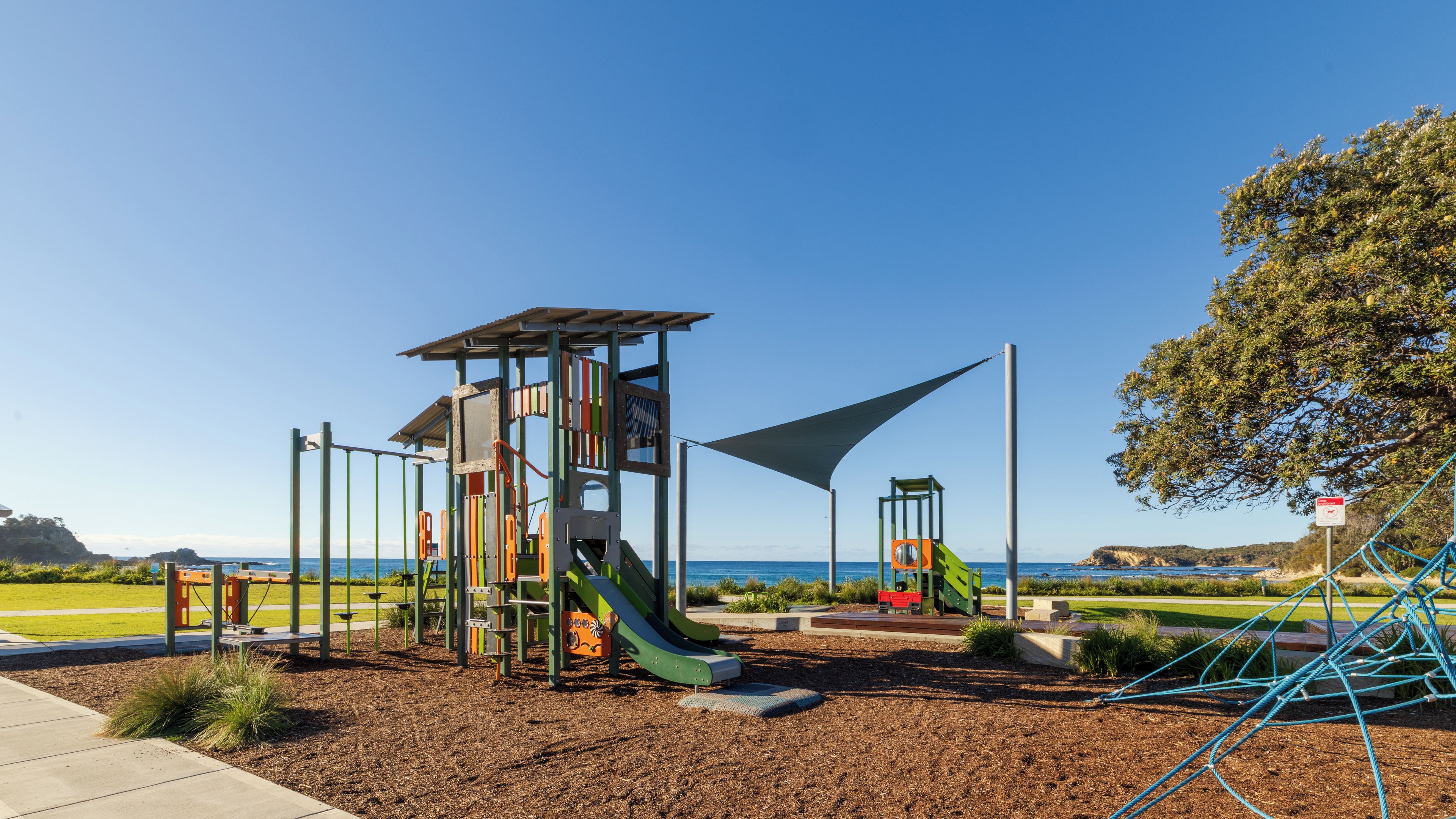 Un parque infantil con tobogán, estructuras para escalar y una zona con sombra.