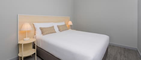 A neatly made bed with a wooden headboard, two bedside tables with lamps, and a light-colored carpet.