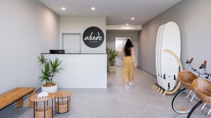 A reception area with a modern design, including a reception desk, potted plants, and a surfboard rack. - Abode Hotel Malua Bay (Malua Bay)