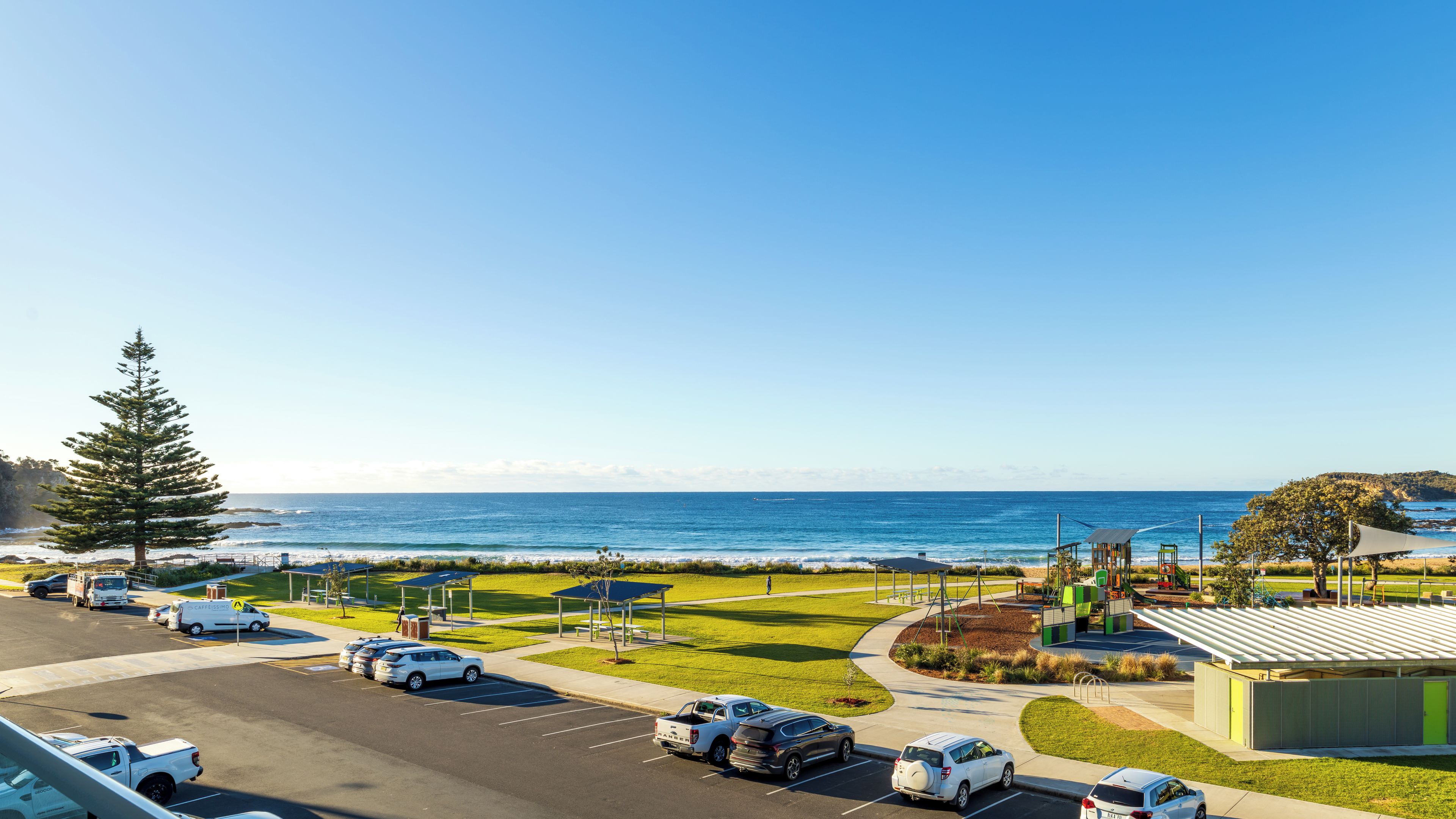 A parking lot with vehicles, a grassy area, and a view of the ocean.