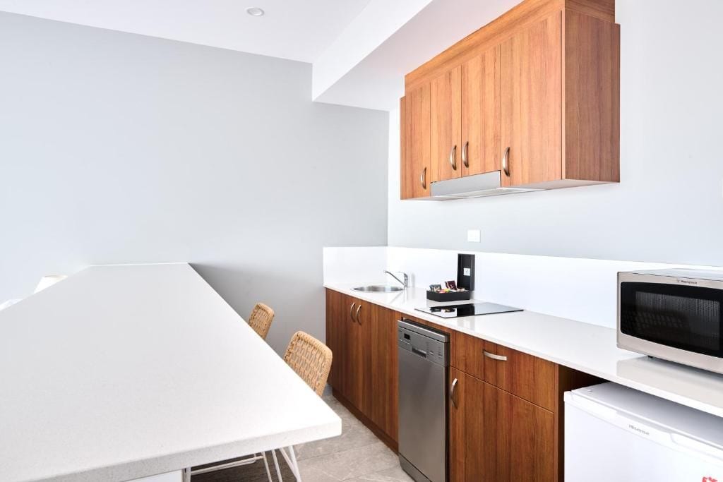A modern kitchen with wooden cabinets, a white countertop, a dishwasher, and a microwave.
