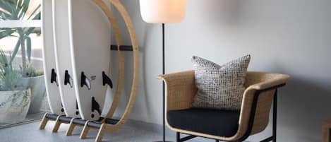 Un interior moderno con una silla de mimbre, una lámpara de pie y tablas de surf apoyadas en una pared.