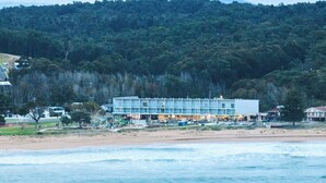 A beachfront hotel with a two-story structure, a sandy beach, and a forested hill in the background. - Abode Hotel Malua Bay (Malua Bay)