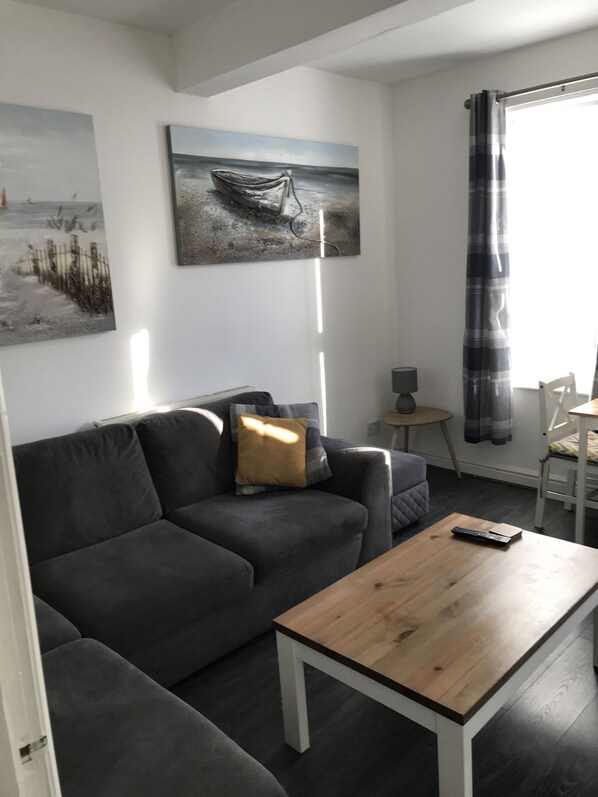 Ett modernt vardagsrum med en grå soffa, ett soffbord i trä och en tavla med ett motiv av en båt på väggen.