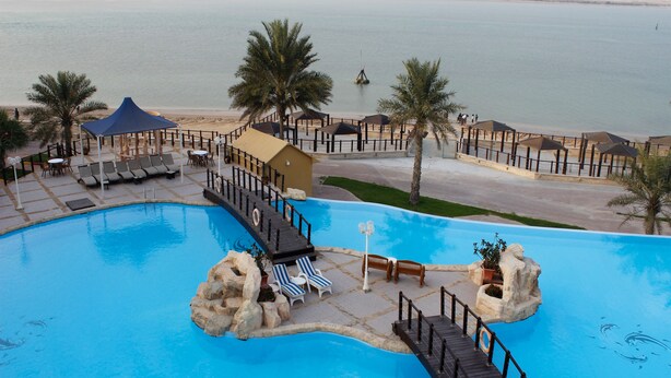 A resort pool with a wooden deck, lounge chairs, and palm trees. - Tio Sea Resort (Al Khor)