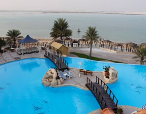 A resort pool with a wooden deck, lounge chairs, and palm trees. - Tio Sea Resort (Al Khor)