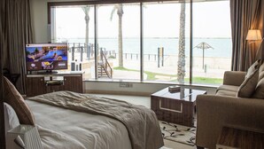 A hotel room with a large window, a bed, a TV, a desk, and a chair. - Tio Sea Resort (Al Khor)