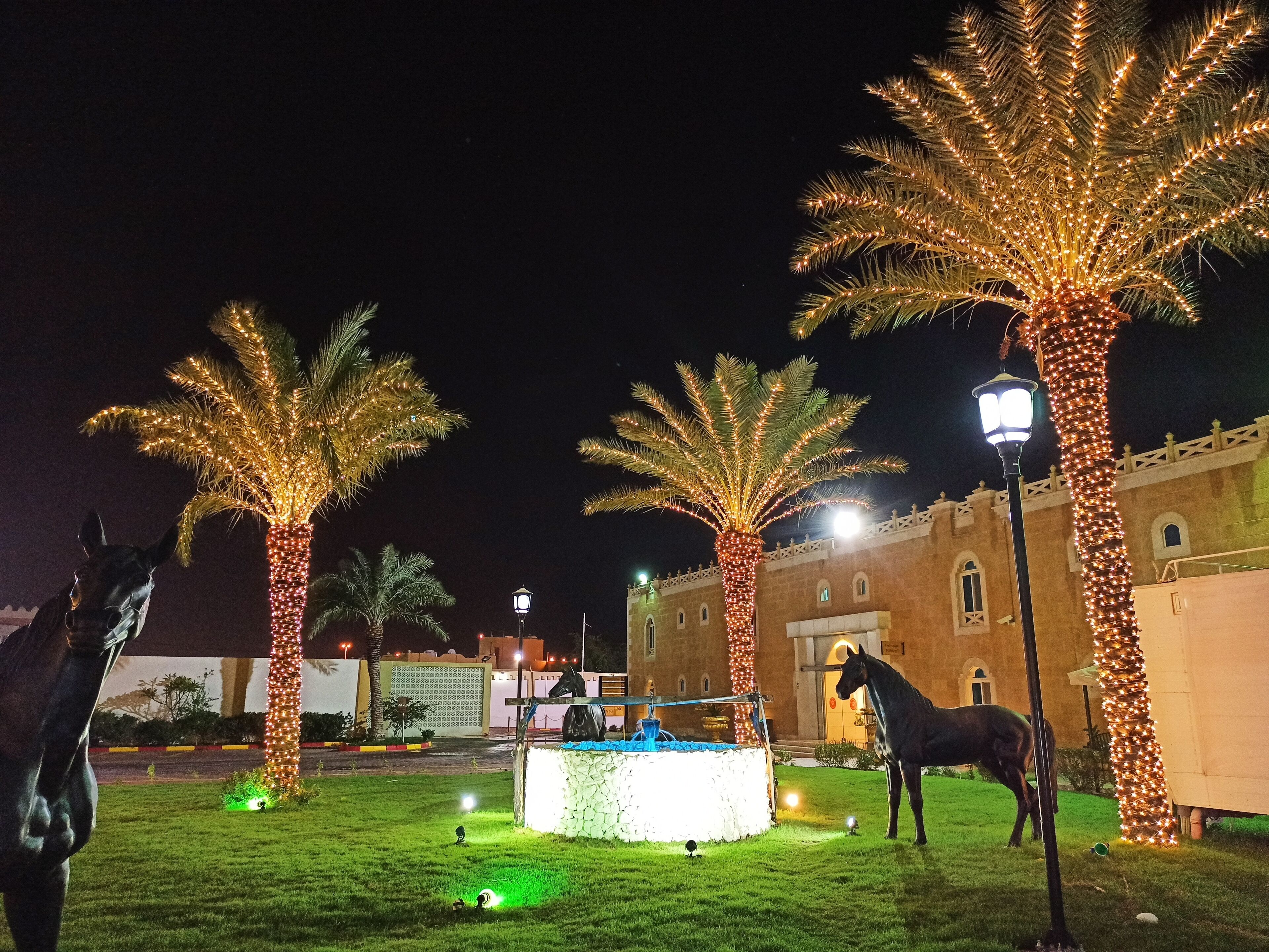A courtyard with palm trees, a fountain, and horse statues.