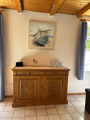 Un meuble en bois orné de sculptures complexes, un tableau encadré représentant un bateau sur une plage et une petite sculpture de poisson placée sur le dessus.