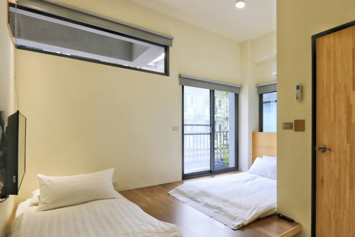 Habitación de hotel con dos camas, una puerta de madera y un ventanal corredero que da a un balcón.