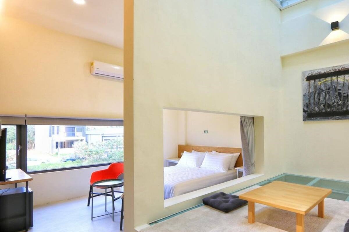 Una habitación de hotel moderna con una cama, una mesita, una silla y un ventanal que ofrece vistas al exterior.