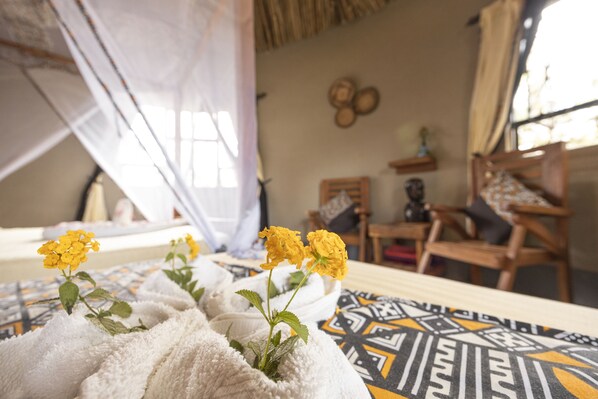 A room with a bed covered in white towels, a patterned rug, and a window with a mosquito net.