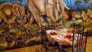 A dining area with a mural of elephants and lions, a table set with plates, glasses, and cutlery.