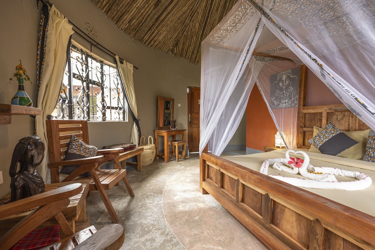 Una habitación con una cama bajo un dosel, muebles de madera, una ventana con cortinas y una estantería con un jarrón.