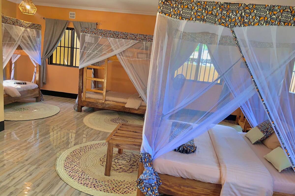 Una habitación con dos camas, cada una con dosel, un banco de madera y una alfombra estampada.