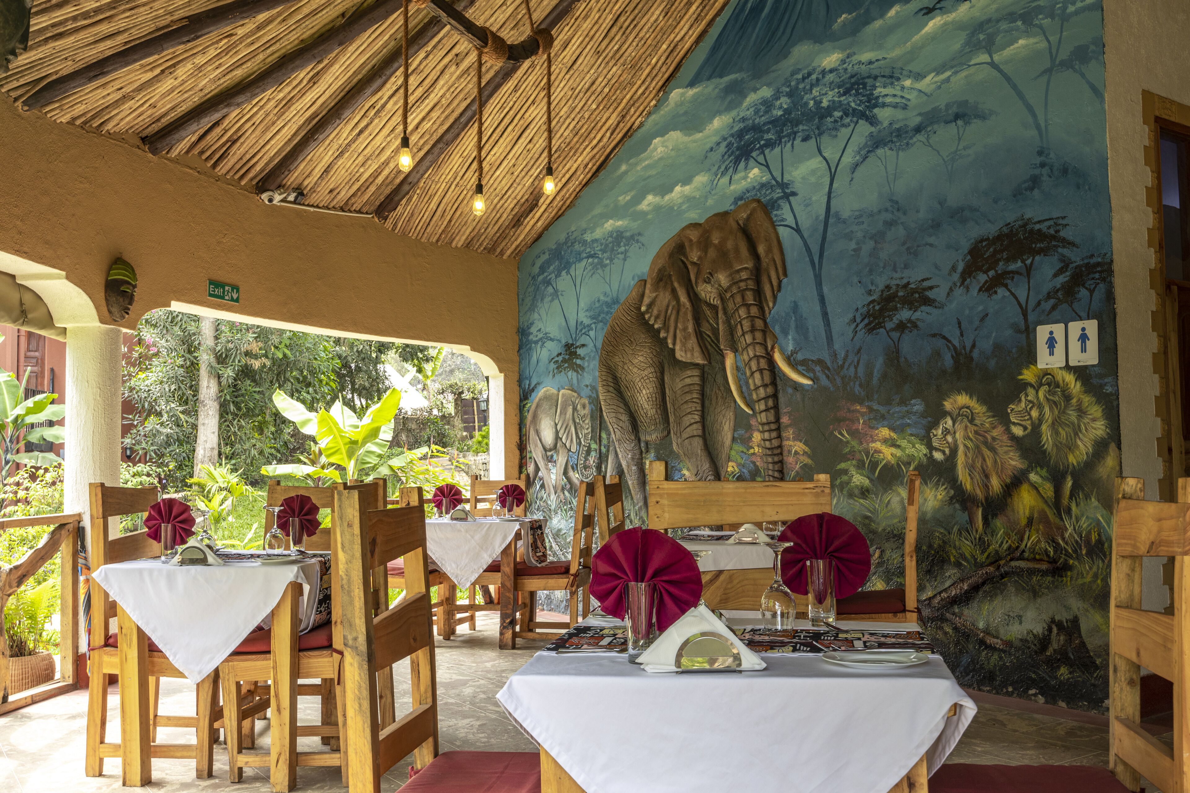 Een restaurant met houten meubels, witte tafellaken en een muurschildering van een olifant.