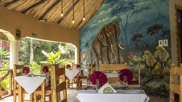 Een restaurant met houten meubels, witte tafellaken en een muurschildering van een olifant.
