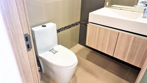 A small, modern bathroom with a white toilet, a wooden cabinet, and a tiled backsplash. - Laguna Beach Resort 1 Jomtien (Pattaya)