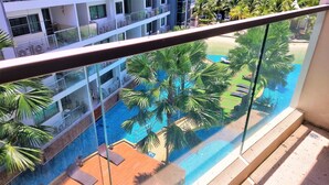A balcony with a view of a swimming pool surrounded by palm trees and a multi-story building with balconies.
