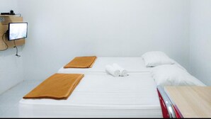 Ein Einzelbett mit weißer Bettwäsche, zwei braune Handtücher, ein Holznachttisch und ein an der Wand befestigter Fernseher.