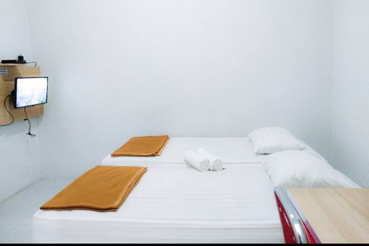 A single bed with white bedding, two brown towels, a wooden side table, and a television mounted on the wall.