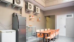Eine moderne Küche mit Kühlschrank, Mikrowelle und zwei Wand-Klimaanlagen. Ein Esstisch mit orangefarbenen Stühlen und ein kleines Schränkchen mit Glastüren sind ebenfalls vorhanden.