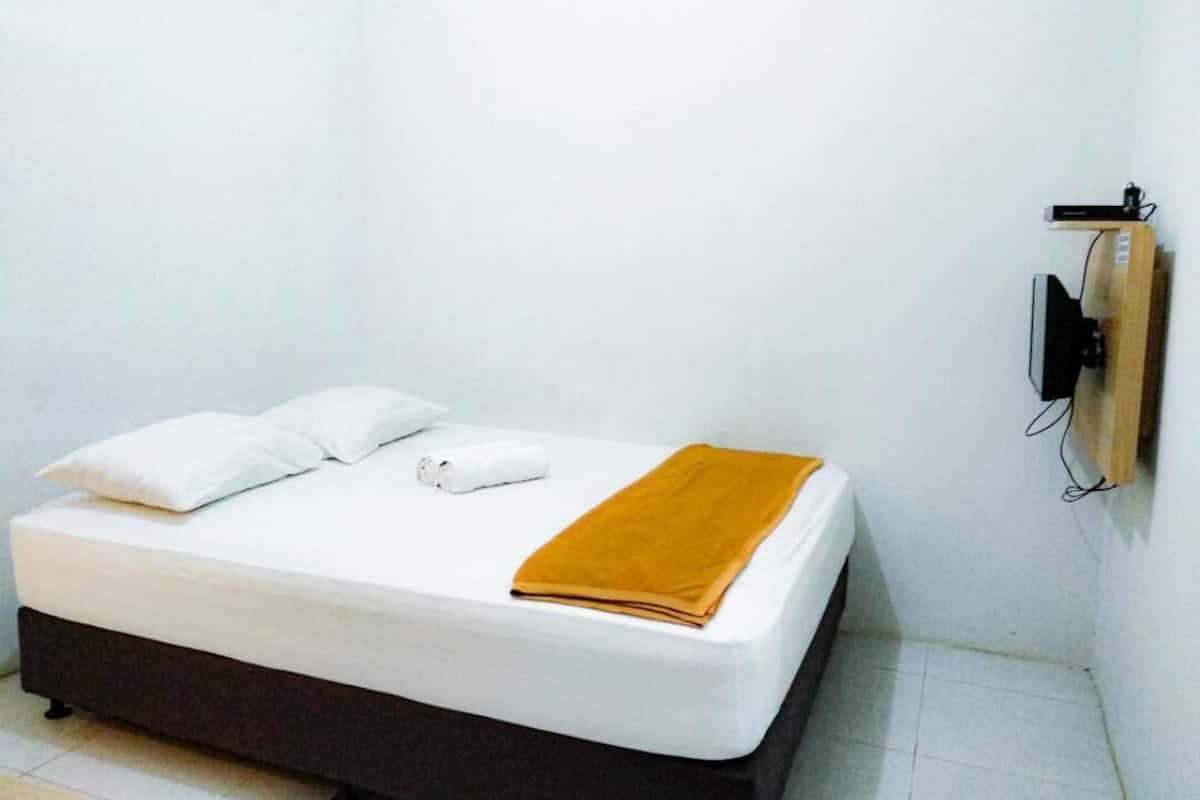 A single bed with white bedding and a mustard-colored blanket, a white pillow, and a rolled towel.
