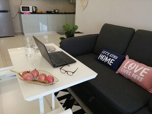 A living room with a white coffee table, a laptop, a basket of apples, a pair of glasses, and a couch with decorative pillows.