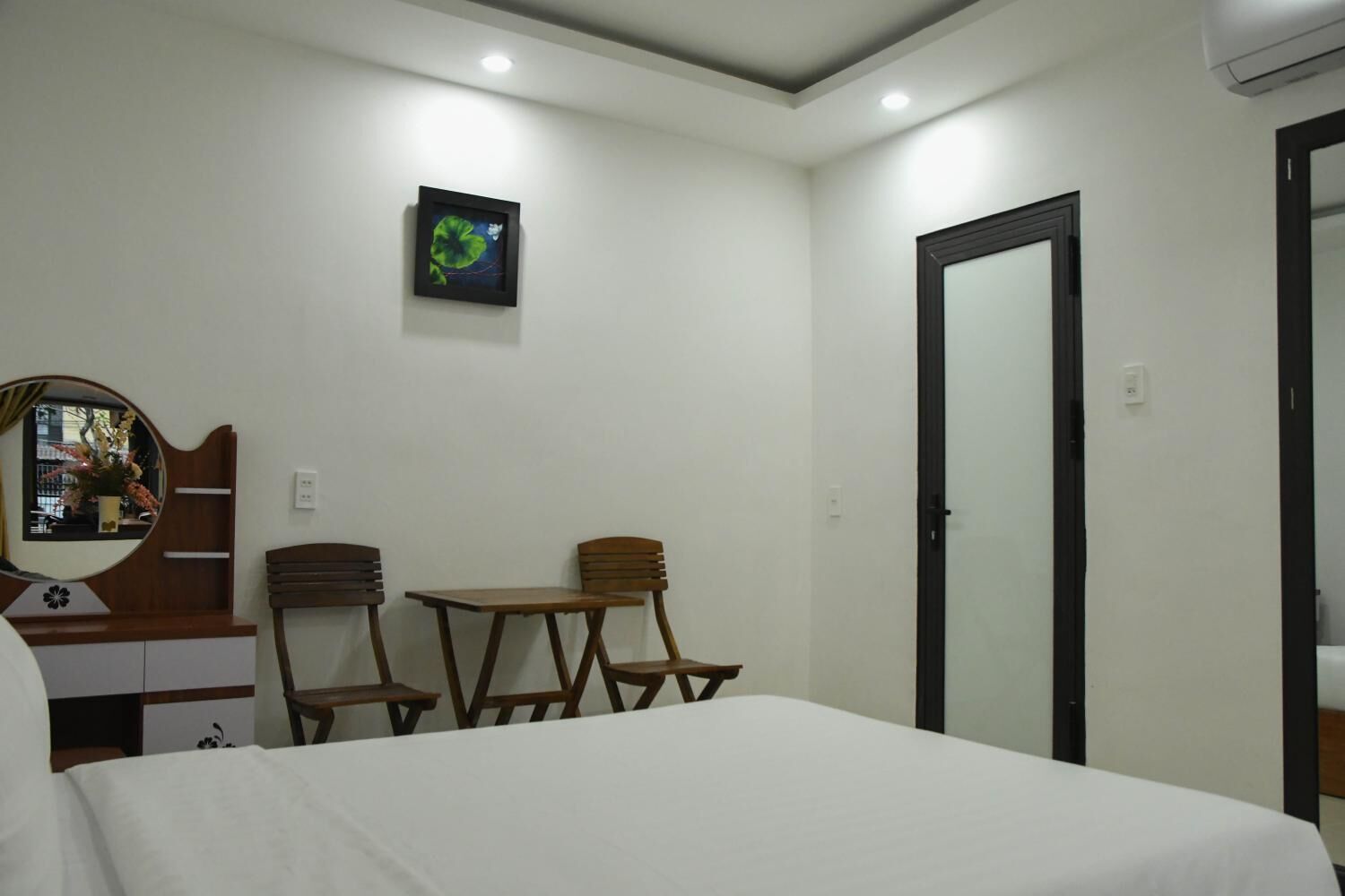 A hotel room with a bed, two wooden chairs, a small table, a mirror, and a picture on the wall.