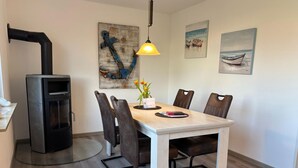 A dining area with a wooden table, six chairs, a black stove, and artwork on the walls. - House Wattkieker, Germany (Wangerland)