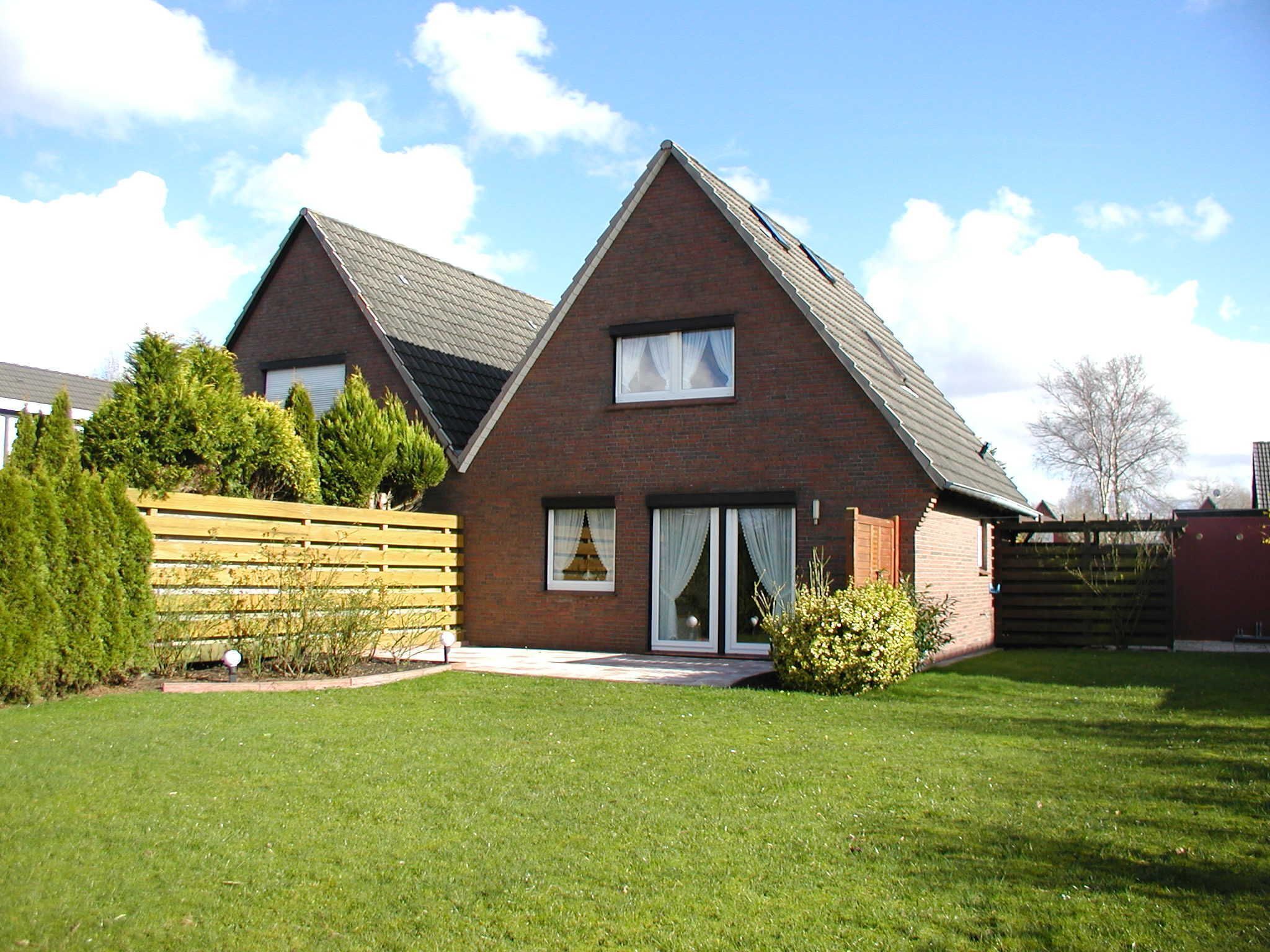 A two-story brick house with a sloped roof, large windows, and a fenced yard.