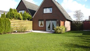 A two-story brick house with a sloped roof, large windows, and a fenced yard. - House Wattkieker, Germany (Wangerland)
